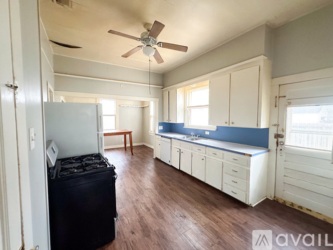 A room with a fan, a fridge, and a suitcase.