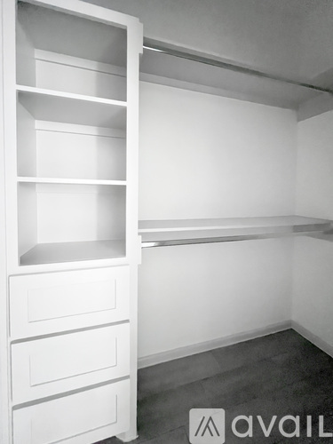A white shelving unit with drawers is in a room with a grey floor.