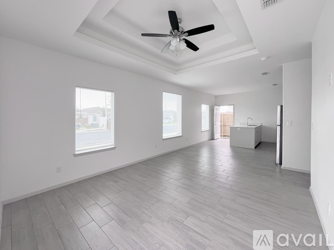 A spacious room with a ceiling fan and light, large windows, and a tiled floor.