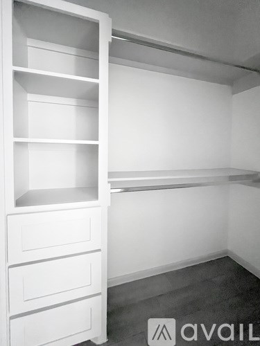 A white shelving unit with drawers is in a room with a grey floor.