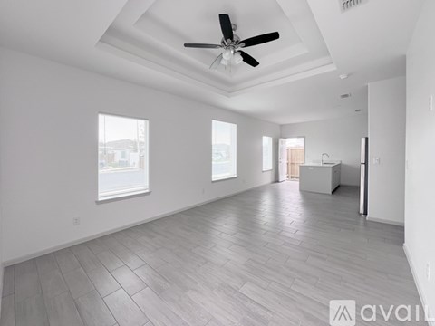 A spacious room with a ceiling fan and light, large windows, and a tiled floor.
