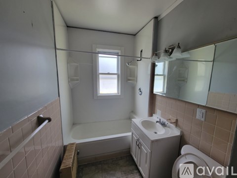 A bathroom with a tub, sink, mirror, and window.