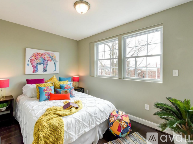 A bedroom with a bed, pillows, a blanket, a lamp, a potted plant, and a framed picture on the wall.