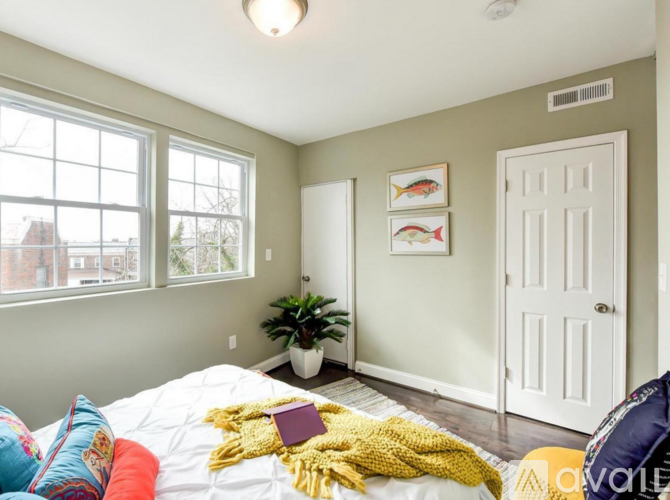 A bedroom with a bed, pillows, a blanket, a potted plant, and pictures on the wall.