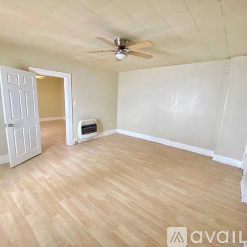A room with a wooden floor and white walls, with a doorway leading to another room.