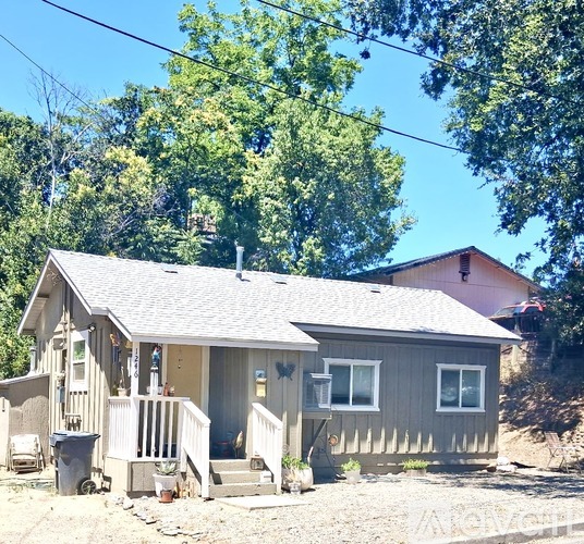 A small house with a porch and a gravel driveway.