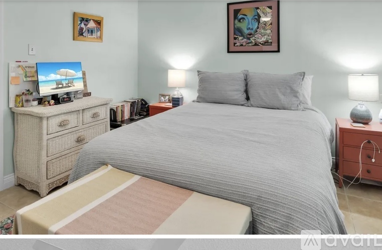 A bedroom with a bed, nightstand, and a dresser with a computer on top.