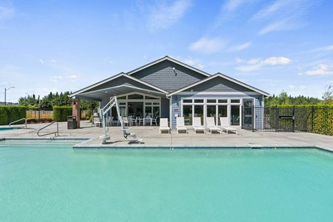 A swimming pool in front of a house with a sunny sky.
