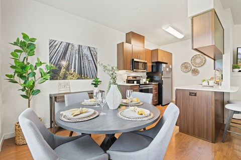 A dining room with a table set for two and a forest picture on the wall.