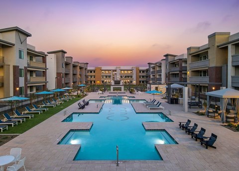 A large swimming pool surrounded by lounge chairs and umbrellas in a residential area.