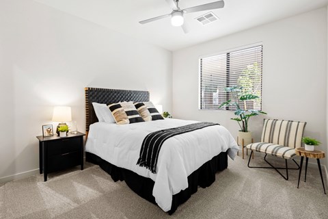A bedroom with a large bed, a chair, and a small table with a lamp on it.
