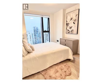 A bedroom with a large bed and a city view through the window.