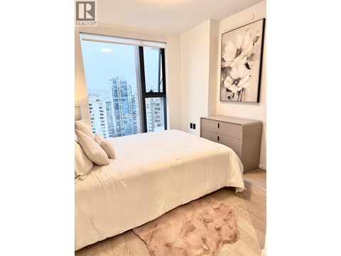 A bedroom with a large bed and a city view through the window.