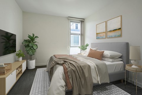 A bedroom with a bed, a nightstand, a window, and a plant.