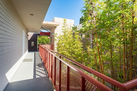 A balcony with a red railing and a view of a building and trees.