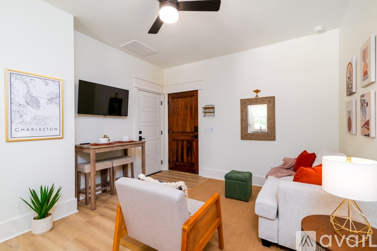 A living room with a white couch, a wooden chair, a white table, a white ceiling fan, a white wall with a map of Charleston on it, a white door, a white lamp, and a white couch with