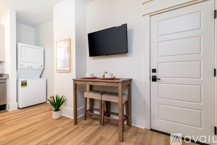 A kitchen with a fridge, a table with two chairs and a TV on the wall.