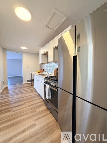 A modern kitchen with a stainless steel refrigerator and wooden flooring.