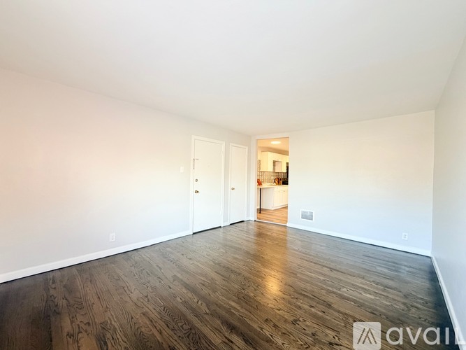 A room with wooden flooring and white walls, with a doorway leading to another room.