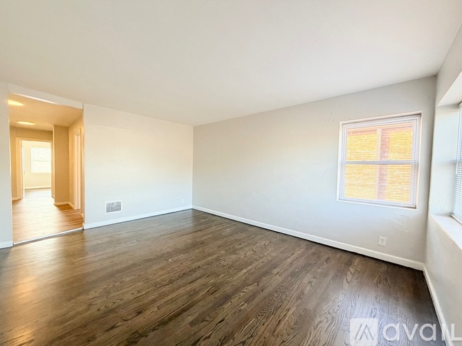 A spacious room with wooden flooring and a window with blinds.