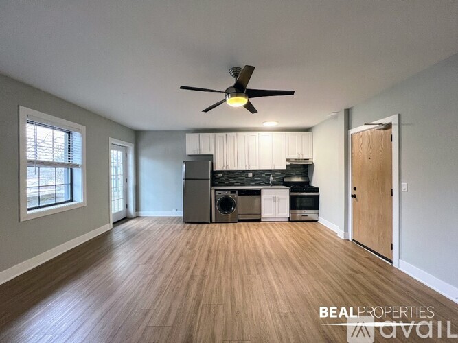 A BEALPROPERTIES sign is on a wall in an empty room with a wood floor and a ceiling fan.