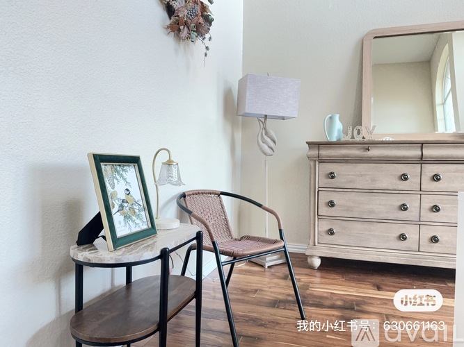 A chair with a woven seat and back is placed in front of a wooden dresser with a mirror above it.