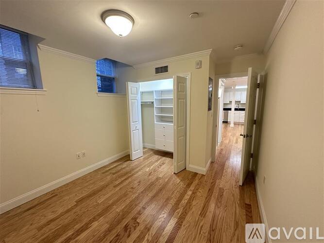 A room with wooden floors and white walls, with a small window on the left wall.