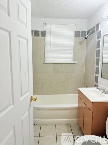 A white door is open to a bathroom with a white tub, sink, and tiled walls.