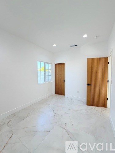 A spacious room with marble flooring and two wooden doors.