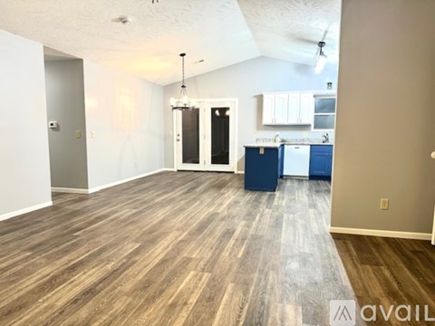 A spacious room with wood flooring and a kitchen area in the background.