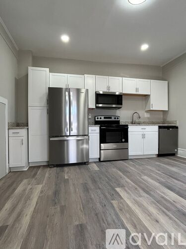 A kitchen with a stove top oven, microwave, refrigerator, and trash can.