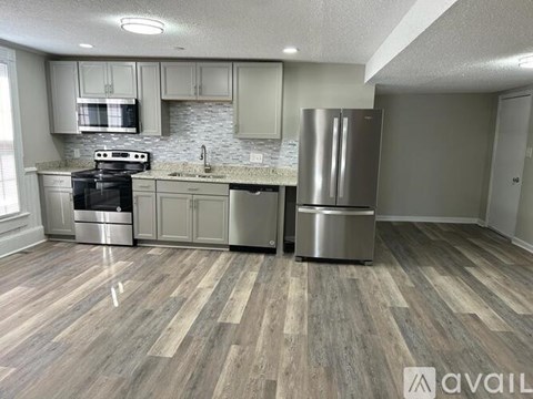 A kitchen with a stove top oven, microwave, refrigerator, and trash can.