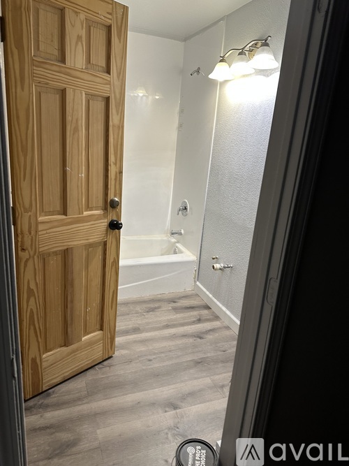 A wooden door is open to a bathroom with a tub and a mirror.