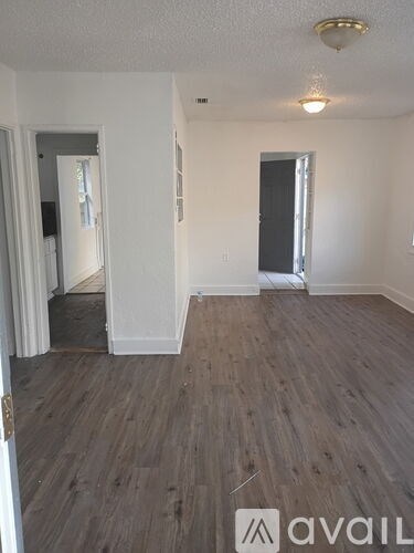 A room with wooden flooring and white walls, with a door on the right and a mirror on the left.