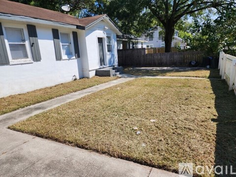 A small white house with a brown roof and a fence surrounding a yard.