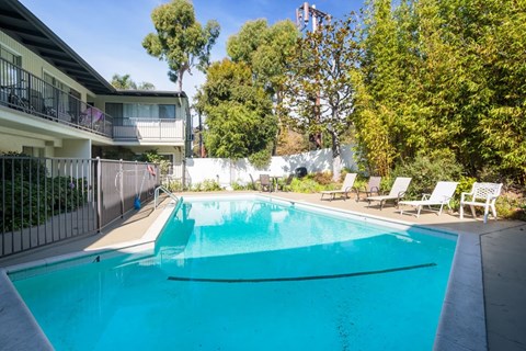 A swimming pool surrounded by trees and chairs.