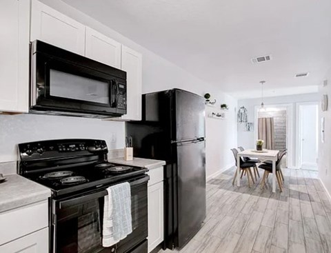 A black refrigerator sits in a kitchen with a white stove and microwave.