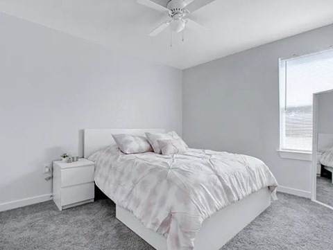 A white bedroom with a bed, nightstand, and window.