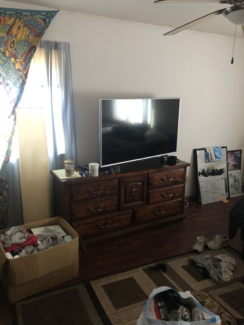 A room with a television, a dresser, and a fan.