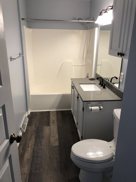 A white toilet is in a small bathroom with a sink and mirror.