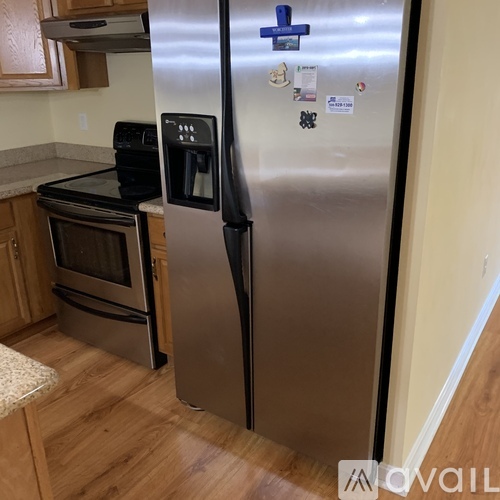 A stainless steel refrigerator with a blue handle and magnets on the door stands in a kitchen.