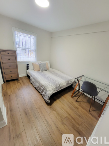 A bedroom with a bed, chair, and wooden floors.
