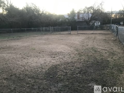 A dirt field with a fence and trees in the background.