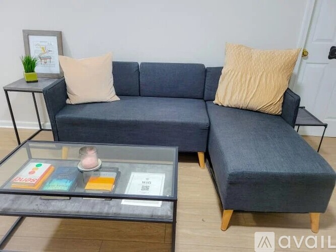 A grey sofa with a glass coffee table in front of it.