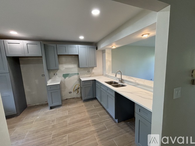 A kitchen with grey cabinets and a white countertop is available for rent.
