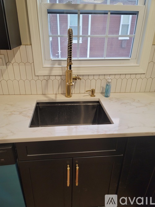 A kitchen sink with a gold faucet and a window above it.