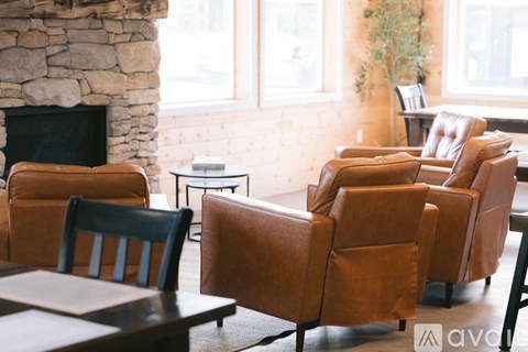 A living room with a stone fireplace and brown leather chairs.