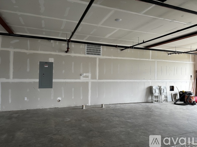 A spacious, empty room with a concrete floor and white walls, featuring a grey electrical box on the wall and a ladder leaning against it.