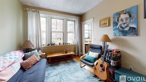 A living room with a blue couch, a guitar, a bookshelf, and a painting on the wall.