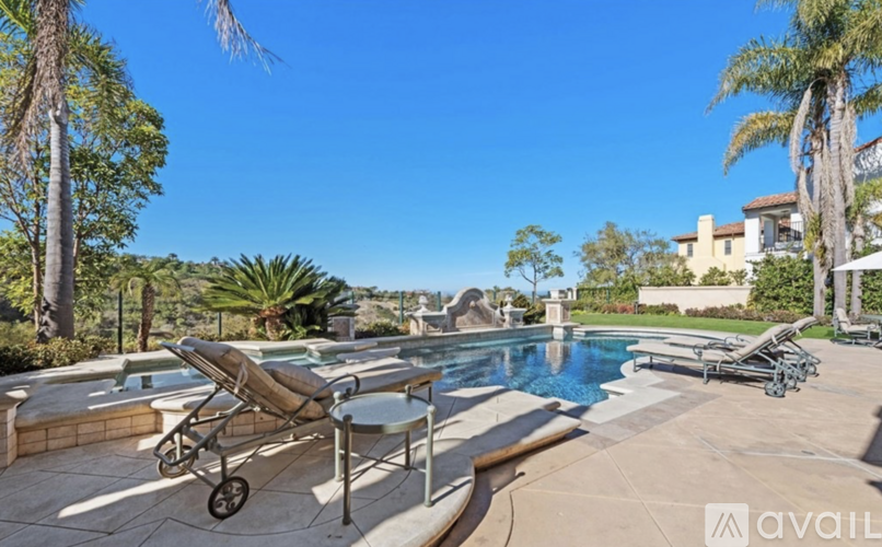 A poolside lounge chair is positioned on a patio with a pool and palm trees in the background.